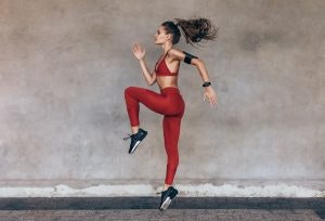 Sportswoman jumping and stretching. Full length of healthy female exercising and jumping outdoors.