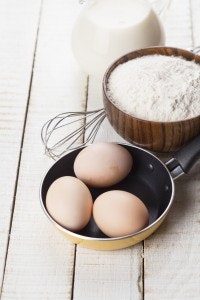 Ingredients for pancakes - eggs, flour, milk on white wooden background. Selective focus.
